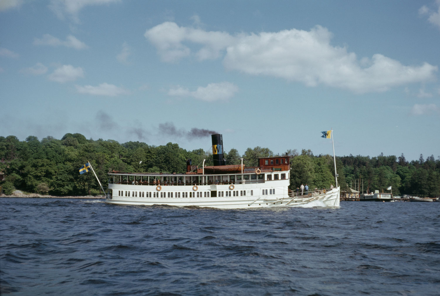 Vitt ångfartyg i skärgårdsmiljö.
